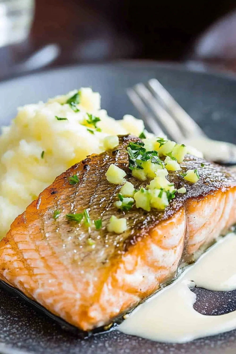 Eine Nahaufnahme eines perfekt gebratenen Lachsfilets, serviert mit cremigem Kartoffelpüree, garniert mit fein gehackten grünen Kräutern und einem Hauch von Sahnesauce.