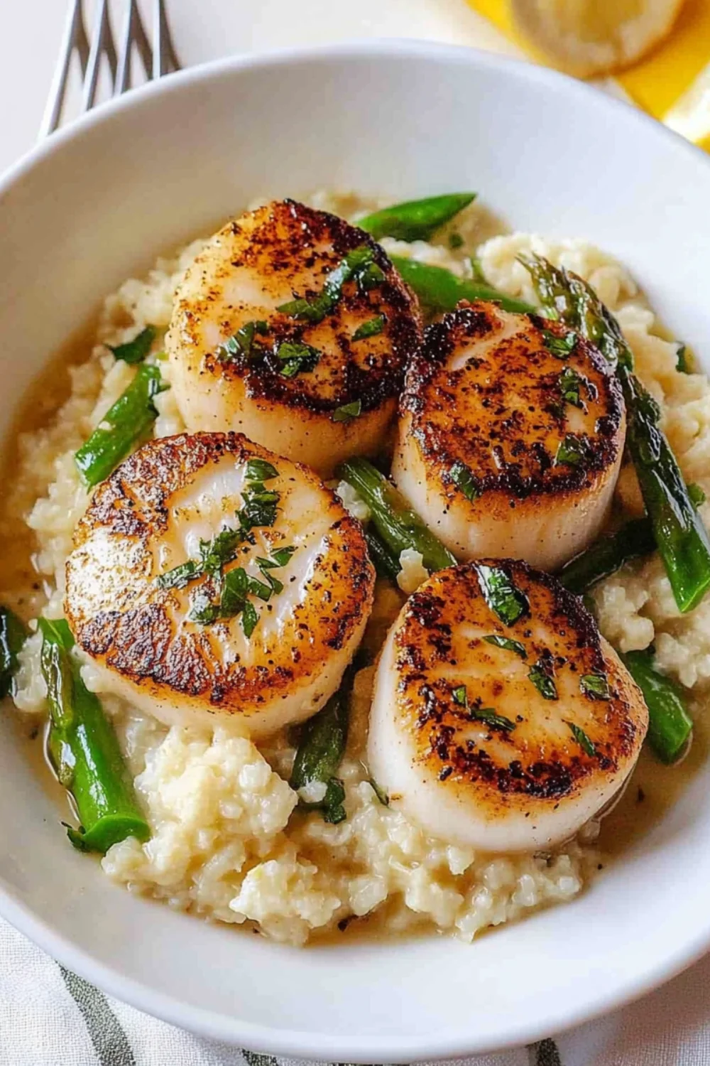 Zart angebratene Jakobsmuscheln auf cremigem Blumenkohl-Risotto, garniert mit grünen Bohnen und frischen Kräutern.